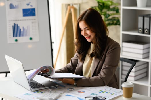 Charming asian woman startup business founder using laptop computer, working with reports at workplace.