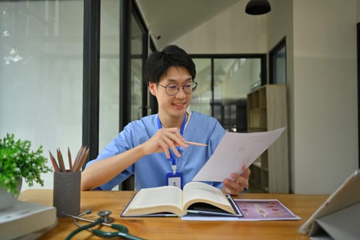 Young surgeon wearing blue scrubs holding and showing digital tablet with blank screen. Healthcare and medical concept.