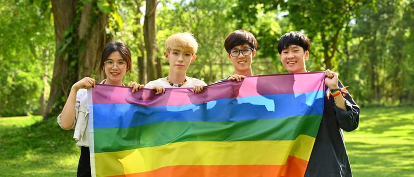 LGBTQ community, freedom, solidarity and equal rights. Image of young people with LGBTQ pride flag, standing in public park.