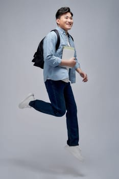 Full length of a smiling young asian man carrying backpack isolated, holding books, jumping 