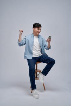Young Asian man play game on mobile phone application and raising his arm up with celebrating success