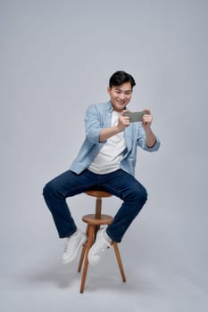 Full body profile side photo of young man sit on a stool play game cellphone over white background