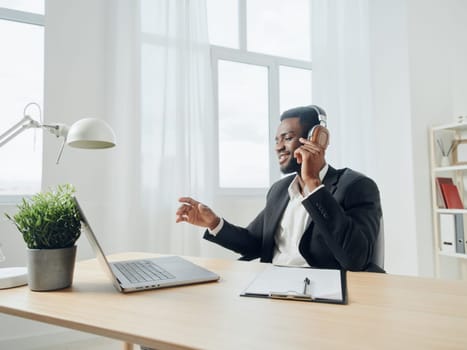 An African-American man sits at his desk in front of his laptop, wearing headphones and chatting on a video call, listening to music. The concept of student business training and online work. High quality photo