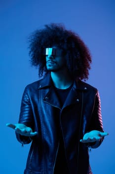 Portrait of fashion man with curly hair with stylish glasses on blue background multinational, colored light, black leather jacket trend, modern concept. High quality photo