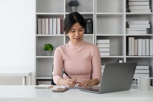 Young woman student busy study make notes in notebook and using laptop concentrated online training course technology education..