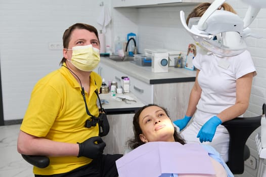 Professional male dental hygienist and a patient look at a screen broadcasting an x-ray image of the oral cavity and teeth. Happy young woman in dentist chair having dental checkup at dentistry clinic