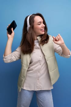 cheerful young lady brunette dances listening to music in headphones on a studio background.