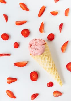 Strawberry ice cream in a waffle cup in the form of a cone, ice cream lies on a white table along with slices of fresh strawberries. Vertical photo