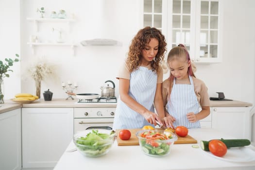 Mommy teaching her teen daughter to cook vegetable salad in kitchen, close up