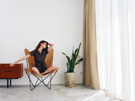 Woman sitting in a leather armchair near the window smiling , modern stylish interior Scandinavian lifestyle, copy space. High quality photo
