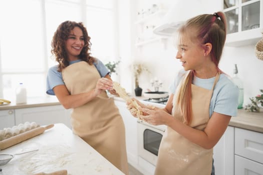 Teen girl helping her mom to cook dough in their kitchen at home, close up