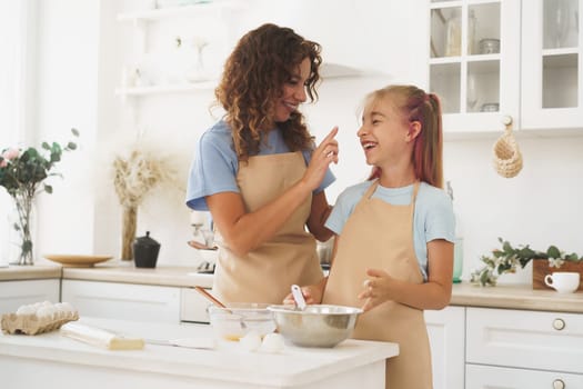 Teen girl helping her mom to cook dough in their kitchen at home, close up