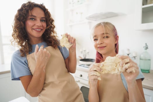 Teen girl helping her mom to cook dough in their kitchen at home, close up