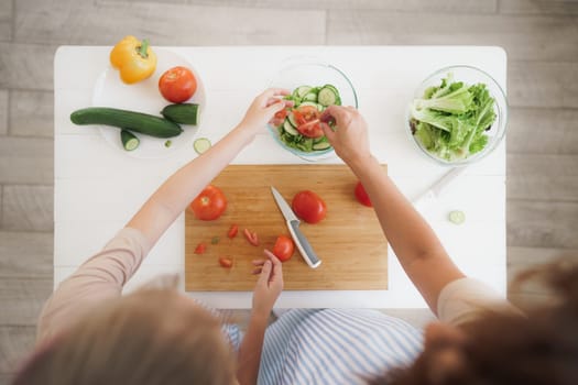 Close up photo of a woman and girl cutting vegetables for salad in kitchen