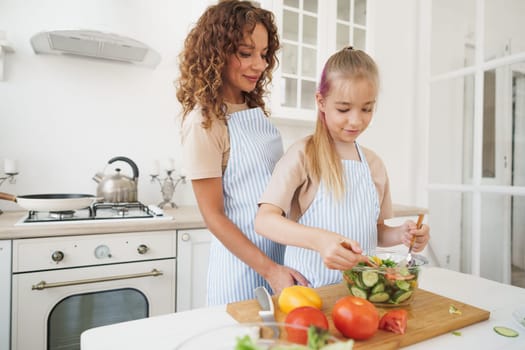 Mommy teaching her teen daughter to cook vegetable salad in kitchen, close up