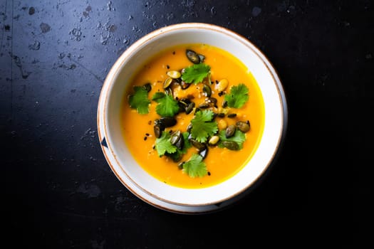 Pumpkin and carrot soup with cream and parsley on a dark wooden background