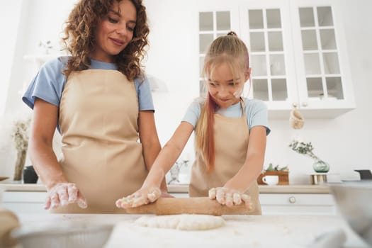 Teen girl helping her mom to cook dough in their kitchen at home, close up