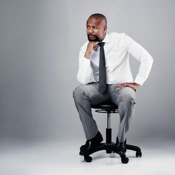 The price of success is hard work and determination. Studio shot of a corporate businessman sitting on a chair against a grey background