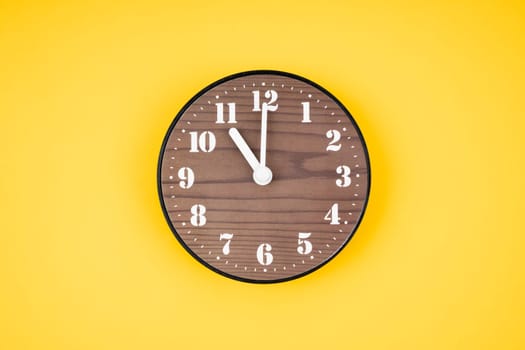 Retro wooden clock at 11 O' clock on yellow color background.