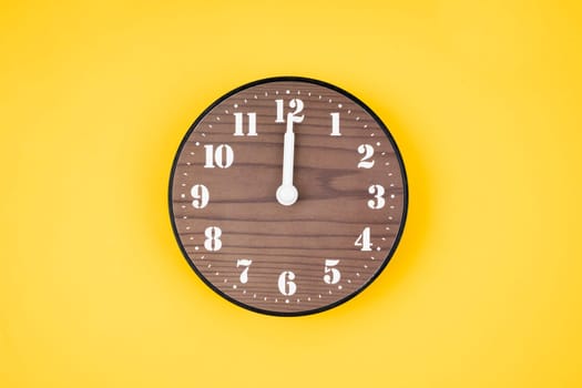 Retro wooden clock at 12 O' clock on yellow color background.