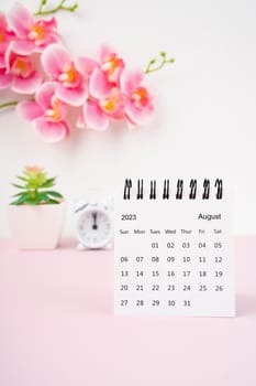 August 2023 desk calendar and pink orchid with alarm clock.