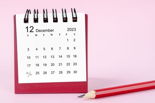 December 2023 desk calendar and wooden pencil on pink color background.