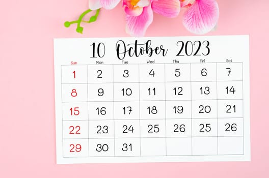October 2023 calendar page and pink orchid on pink background.
