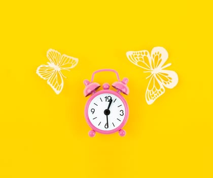 Pink alarm clock and paper butterflies on a yellow background.