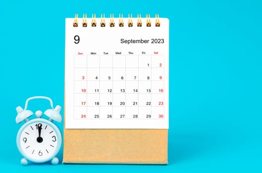 September 2023 Monthly desk calendar for 2023 year and alarm clock on blue background.