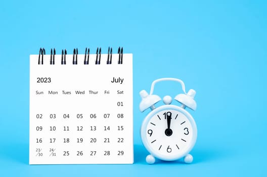 July 2023 desk calendar and alarm clock on blue color background.