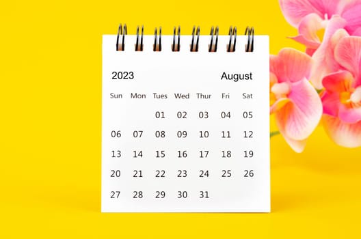 August 2023 calendar desk and pink orchid on yellow background.