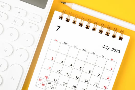 July 2023 Monthly desk calendar for 2023 year and calculator with pen on yellow background.