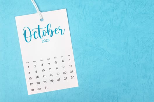 2023 October calendar page hanged on white rope on blue background.