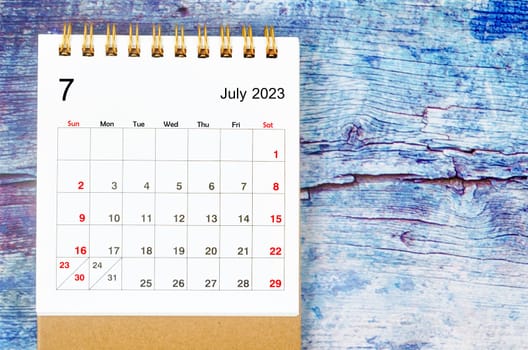 July 2023 Monthly desk calendar for 2023 year on old blue wooden background.