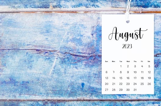 August 2023 calendar page hanged with white rope on old blue wooden background.