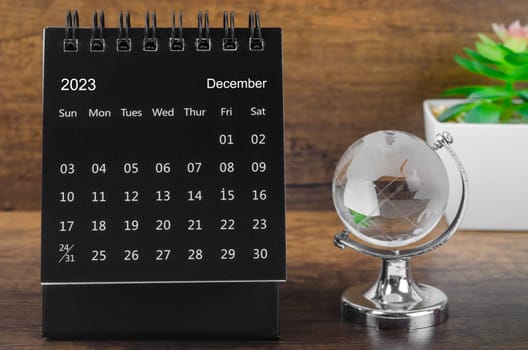 December 2023 desk calendar for 2023 year Black color with a crystal globe against a wooden table background.