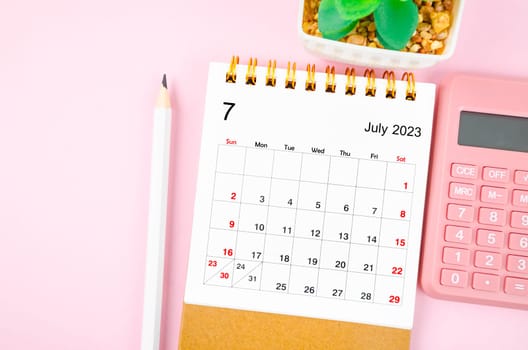 July 2023 desk calendar for 2023 year with calculator on pink color background.