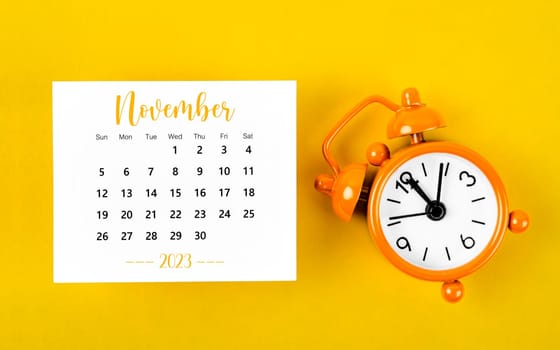 November 2023 Monthly calendar for 2023 year with black colour alarm clock on yellow background.