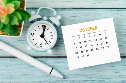 October 2023 Monthly calendar year and alarm clock with pen on blue wooden background