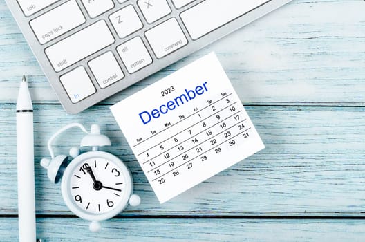 December 2023 Monthly calendar year and alarm clock with keyboard computer on blue wooden background.