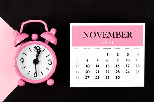 November 2023 Monthly calendar year with alarm clock on pink and black background.