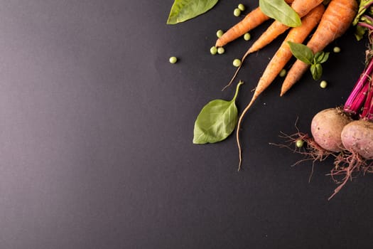 High angle view of carrots and beetroots with green peas and leaf vegetable on black background. unaltered, healthy food, vegetable, raw food, variation and organic concept.