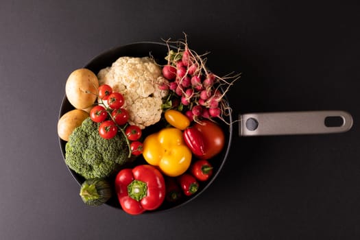 Overhead view of various colorful vegetables in frying pan on black background. unaltered, vegetable, healthy food, raw food, variation and organic concept.