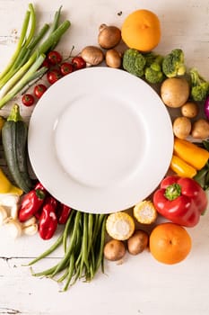 Directly above shot of empty white plate amidst various vegetables and fruits on table. unaltered, vegetable, healthy food, raw food, fruit, variation and organic concept.
