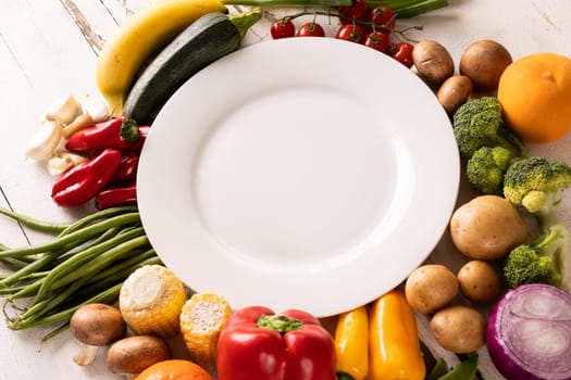 High angle view of empty white plate amidst various vegetables and fruits on table. unaltered, vegetable, healthy food, raw food, fruit, variation and organic concept.