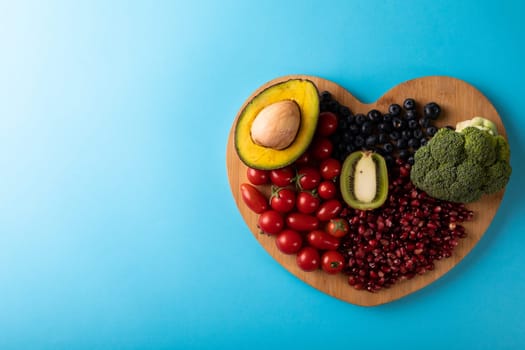 Directly above view of healthy food on heart shaped cutting board over blue background. unaltered, healthy eating, food, organic, copy space.