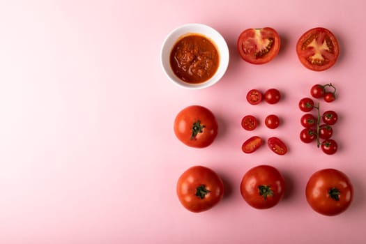 Overhead view of fresh puree in bowl by various red tomatoes by copy space on pink background. unaltered, food, healthy eating, organic concept.