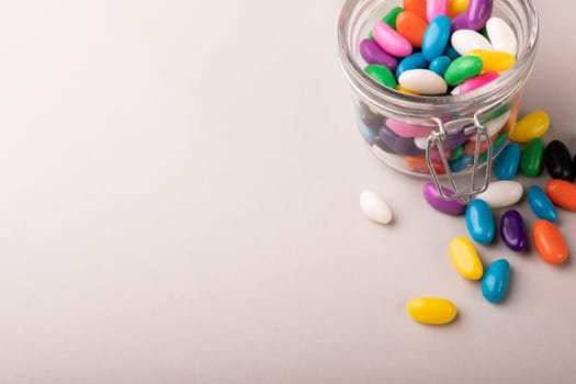 High angle view of copy space with colorful candies and open glass jar on white background. unaltered, sweet food and unhealthy eating concept.