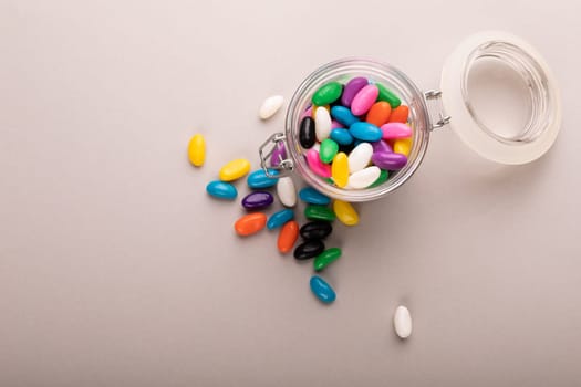 Overhead view of open glass jar with colorful candies by copy space on white background. unaltered, sweet food and unhealthy eating concept.