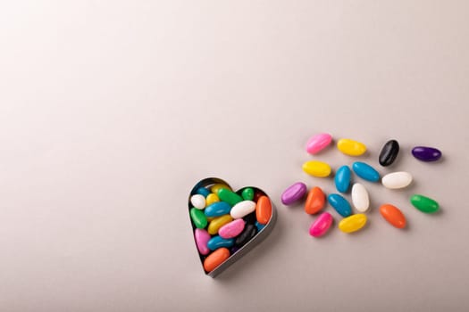 Overhead view of heart shape container with colorful candies by copy space on white background. unaltered, sweet food and unhealthy eating concept.